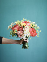 A hand holding a bunch roses, peonies, fresias and camomile