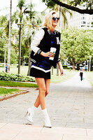 A blonde woman wearing a mini dress, a letterman jacket and white high heels with white socks
