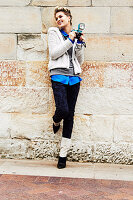 Blonde Frau im Webpelzjacke und Jeans mit Brokatmuster hält Fotoapparat