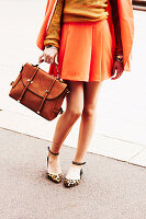 Frau in orangefarbenem Outfit, Schuhe mit Leo-Print und Ledertasche