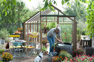 Glass house with seating place and water barrel in the garden