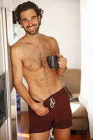A young, topless man holding a cup of coffee