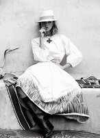 A woman wearing a hat, a white blouse and a white, printed skirt (black-and-white shot)