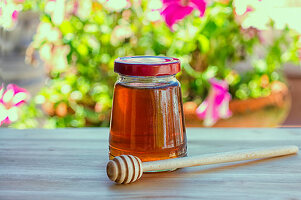 A jar of honey and a honey dipper on a garden table