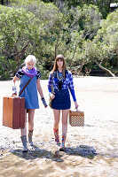 Two young women with suitcases wearing blue outfits and colourful wellie boots