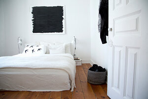 Double bed with white bedspread below black painting in bedroom with wooden floor