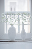 weiße Blumenvasen mit Schleierkraut auf Fensterbank