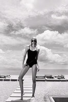 A blonde woman wearing a black bathing suit by a pool (black-and-white shot)