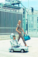 Blonde Frau neben Miniaturwagen mit 'Roboter'