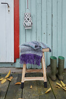 A self-knitted scarf on a wooden stool on a terrace
