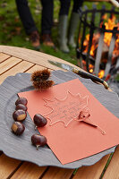 Herbtliche, selbst gemachte Einladungskarte auf Holzplatte mit Kastanien