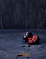Red plums, whole and halved, against a dark background