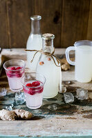 Festive gingerbeer in bottles and glasses served with raspberries on a rustic wooden surface with ice as a gift