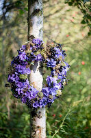 Kranz aus lila Hortensien und schwarzen Johannisbeeren am Baum hängend
