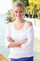 A young blonde woman wearing a white top and a jumper by the sea