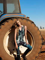 A young woman wearing a top, leggings and boots standing next to a tractor