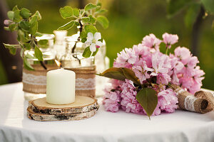 Kerze auf Baumscheibe, Kirschblüten und Pfingstrosen auf Gartentisch