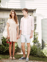 A young woman wearing a light dress and a young man wearing a shirt and shorts in a garden