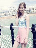 Junge Frau in blau-weiß kariertem Top und rosa Shorts auf der Brücke