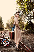 Junge Frau in langem Mantel mit Koffern am Gleis