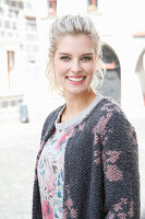 A young blonde woman wearing a pink and grey knitted coat