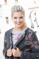 A young blonde woman wearing a pink and grey knitted coat