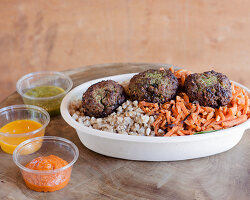 A falafel bowl with vegetables and a trio of dips