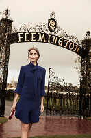 Junge Frau in elegantem blauem Kleid vor dem Pferderennbahn (Flemington Racecourse, Melbourne)