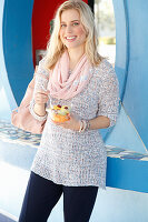 A blonde woman wearing a knitted jumper and dark trousers holding a fruit salad