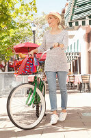 Blonde Frau in Jeans und Strickpulli beim Shopping mit Fahrrad
