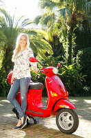 A blonde woman wearing jeans and a blouse leaning on a motor scooter