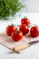 Ganze Tomaten auf Tuch mit Messer vor frischem Thymian