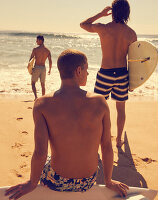 Drei junge Männer mit Badeshorts am Meer