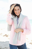 A brunette woman wearing a pink jumper with a grey jumper over her shoulders