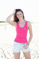 A young woman on a beach wearing a pink top and light shorts