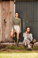 Two women with a dog in front of a wooden door on a farm