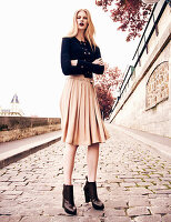 A blonde woman wearing a black jacket and a sand-coloured skirt