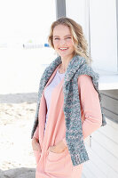 A blonde woman wearing an apricot cardigan with a jumper over her shoulders