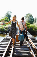 A young couple with a suitcase and a guitar on a railway track