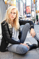 A blonde woman wearing a black blazer and grey jeans sitting on the floor
