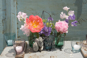 Peonies and sweet peas in bottles in bottle holder decorating table