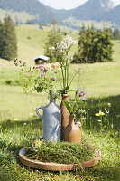 Rampion, lady's mantle, astrantia and marjoram in rustic stoneware jug and swing-top bottles