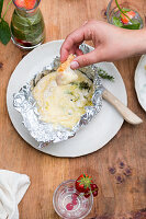 Eating melted cambembert in alumiumfoil with a hand on a table