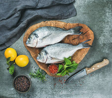 Fresh uncooked sea bream or dorado fish with lemon, herbs and spices in bowls
