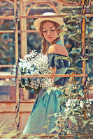 Junge Frau mit Strohhut und Blumenstrauß in blauer Carmenbluse und Rock