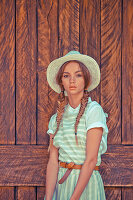 A young woman wearing a hat and a blouse with a striped pinafore dress