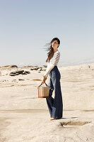 A brunette woman wearing a striped jumper and jeans holding a wicker basket