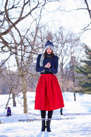A young woman wearing a blue hat and scarf, a blue jumper and a red skirt in a wintery park