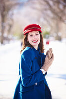 A brunette woman wearing a red hat and a blue coat in a wintery park