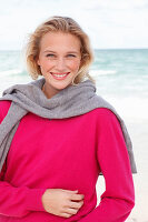 A young blonde woman wearing a pink jumper with a grey jumper over her shoulders